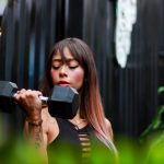 Fitness woman with long hair lifting a dumbbell outdoors, focusing on her strength training.